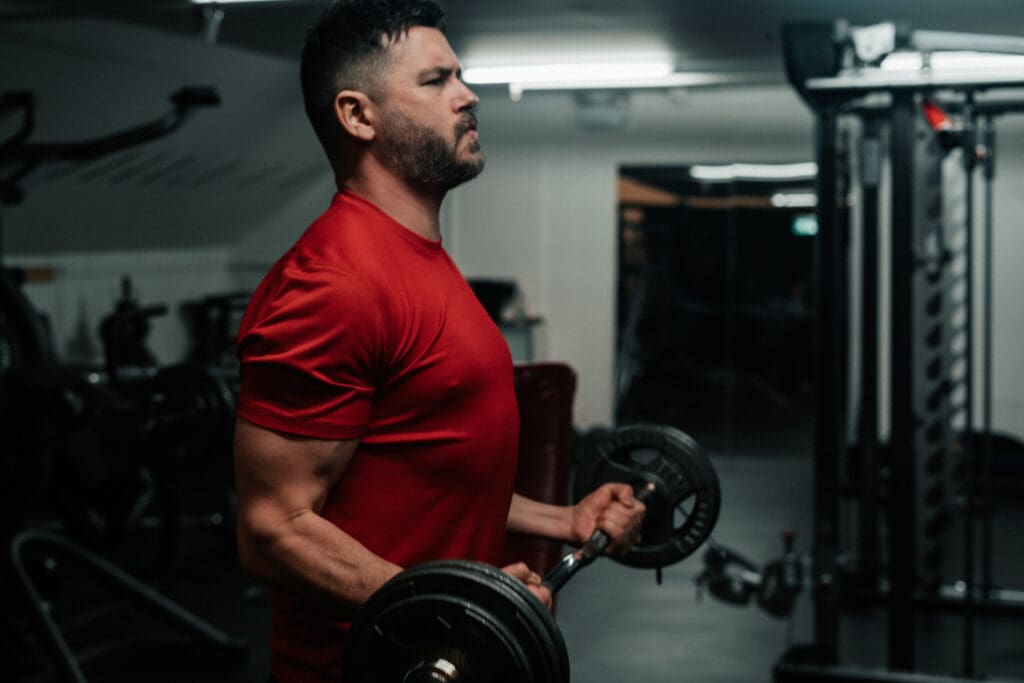 Man in a red shirt performing an EZ-bar curl in a gym