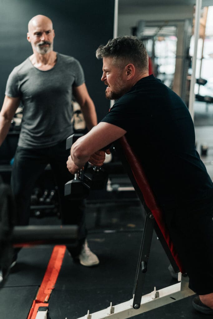 Trainer watching a member perform a dumbbell preacher curl